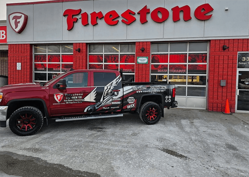 A red truck parked in front of firestone tires.